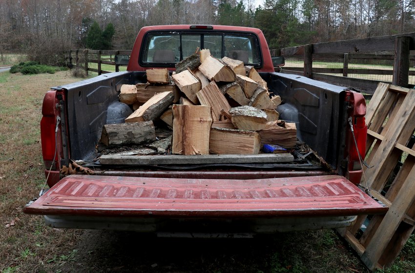 The bed of an old red pickup truck loaded with split logs and wood scraps, tailgate down