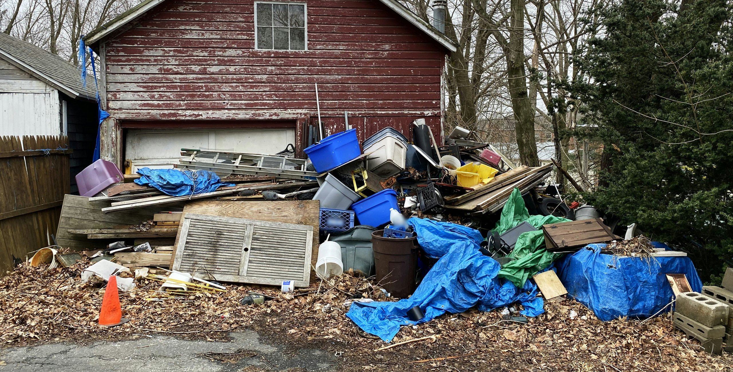 A large pile of household junk, lumber and blue tarps heaped in front of an old red wooden garage